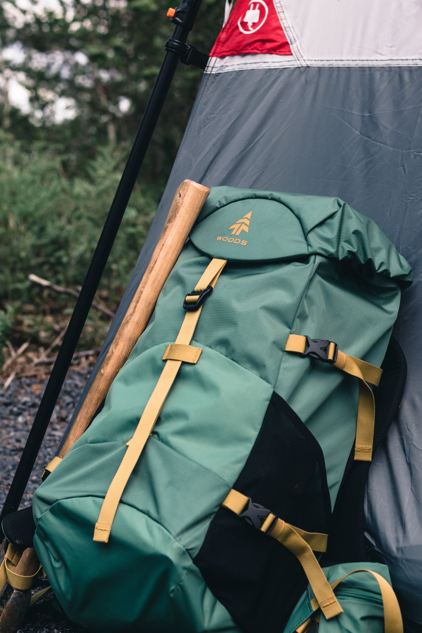 A green backpack resting beside a tent at a forest campsite
