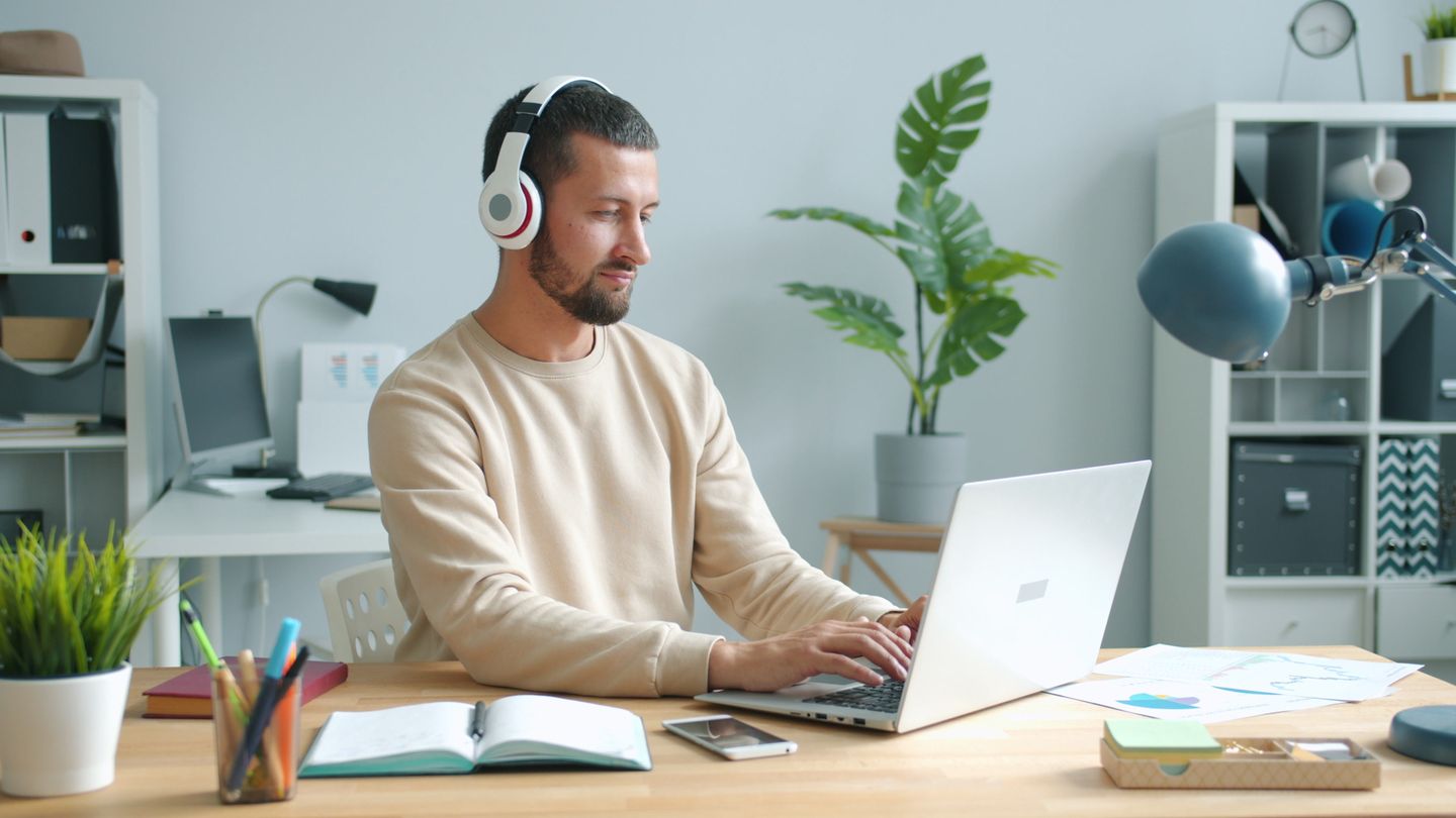 A home worker using headphones at a laptop and wooden desk