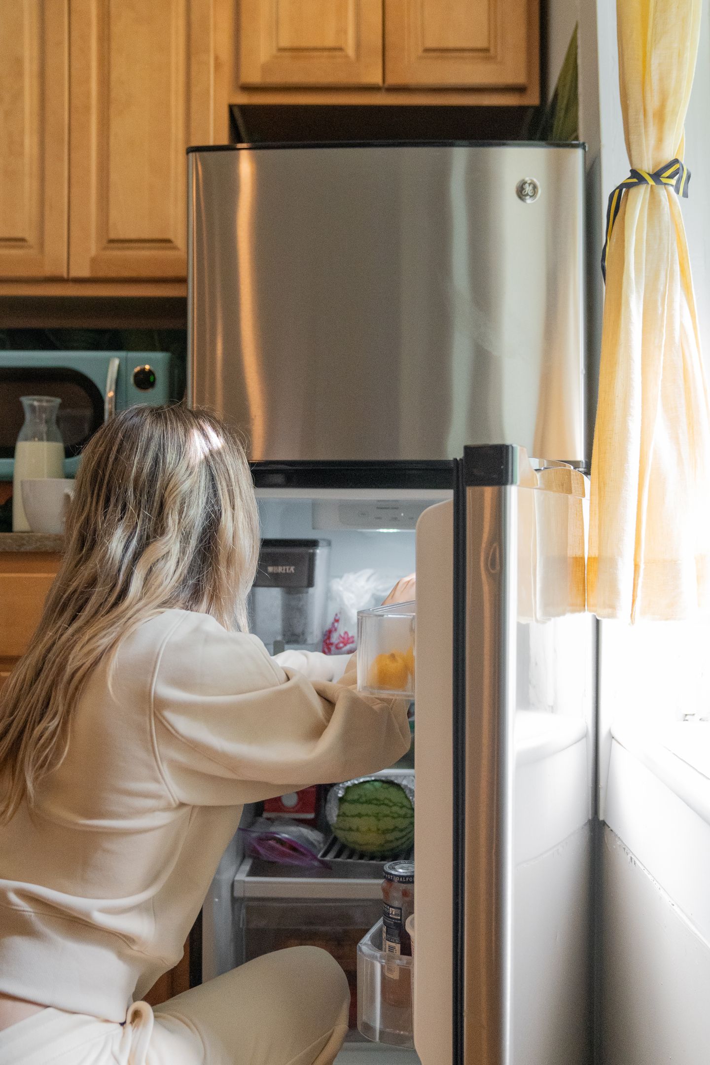 A person reaching into a refrigerator in a bright home kitchen