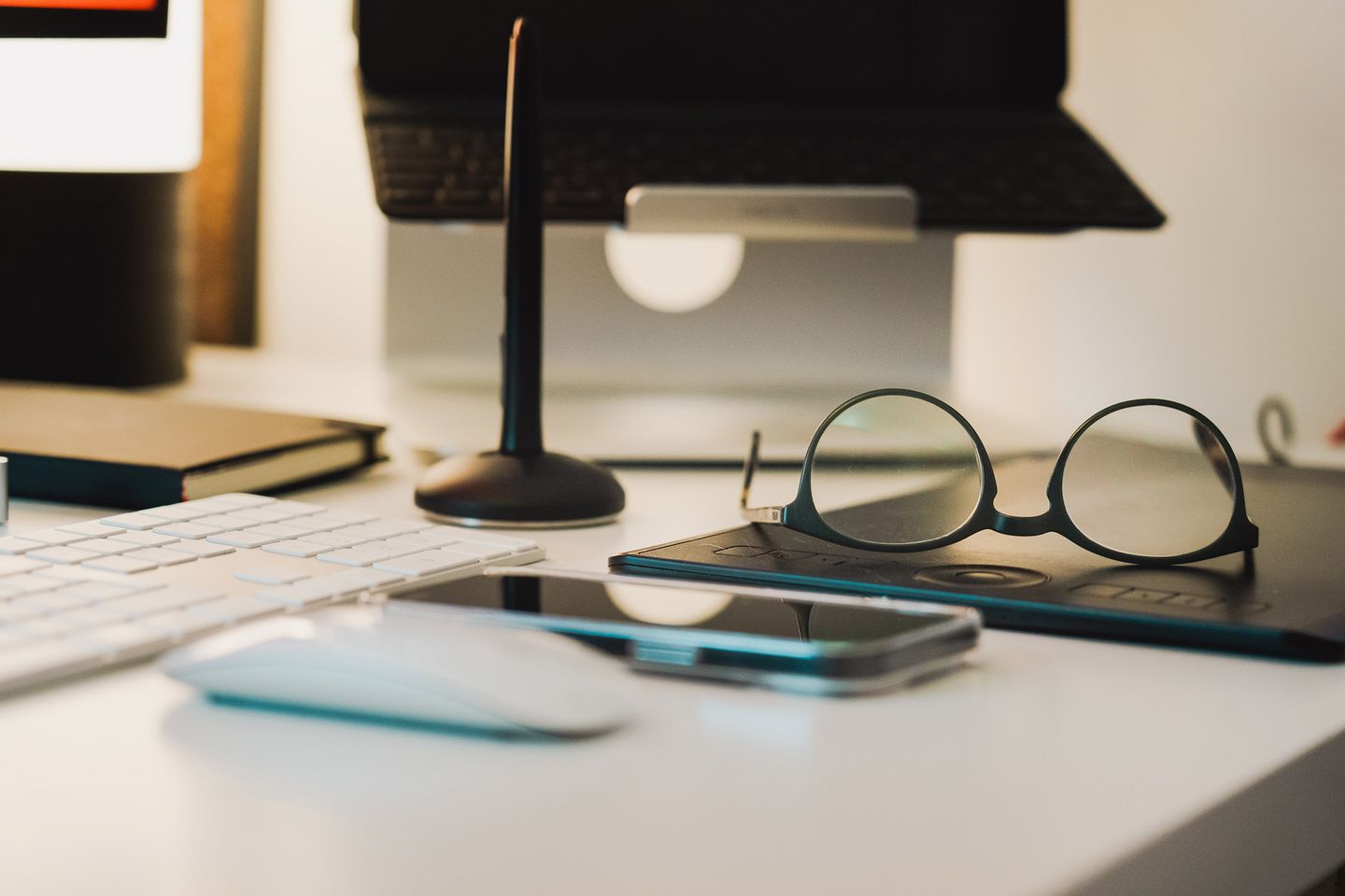 A tidy home-office desk with a laptop, phone, keyboard, and everyday accessories